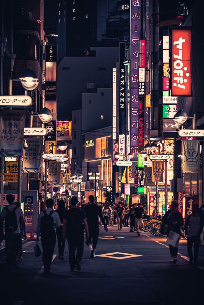 People walking on the street between buildings under commercial billboard ads in Tokyo, Japan.